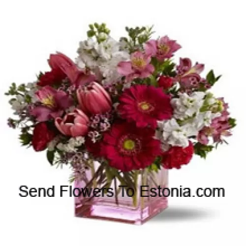 赤いバラ、赤いチューリップ、季節の詰め物を加えたアソートされた花々がガラスの花瓶に美しくアレンジされています